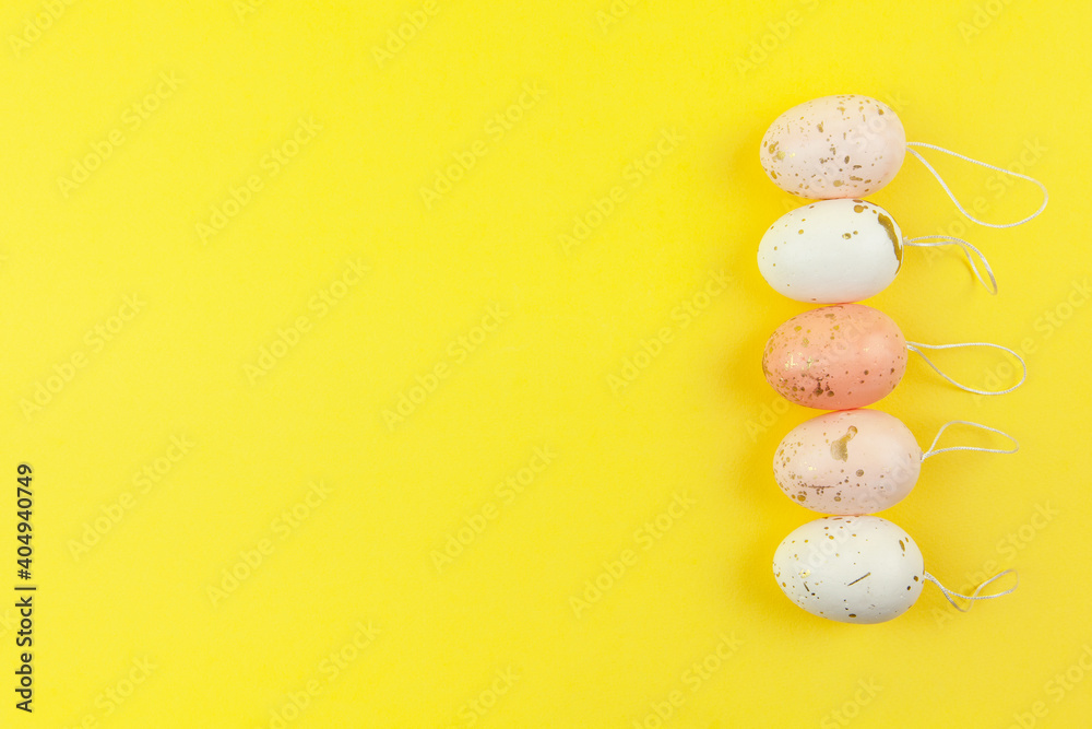 Creatively painted eggs in pastel colors decorated with gold leaf are arranged in row along side edge on yellow background, copy space. Happy Easter, DIY concept, interior decor. Flat lay. Horizontal