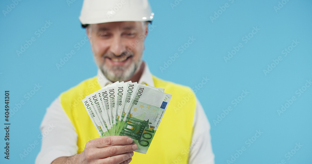Close up of Engineer in uniform and helmet showing euro isolated over blue background. Money and Euro Concept. Close up of Engineer in uniform and helmet showing euro isolated over blue background. Money and Euro Concept.