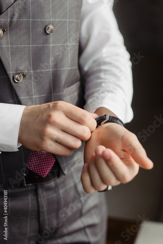 A man fastens his watch on his hand. The groom's wrist is in a suit. Wedding morning. Male business image.