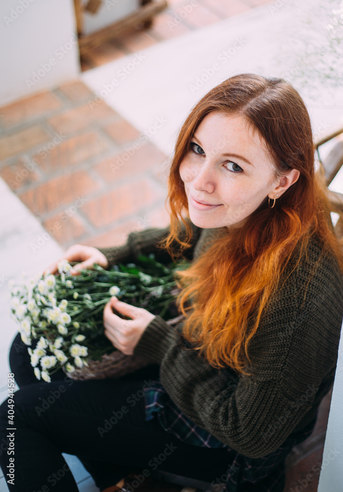 Beautiful ginger young girl in an apron among the flower shop. Spring concept.