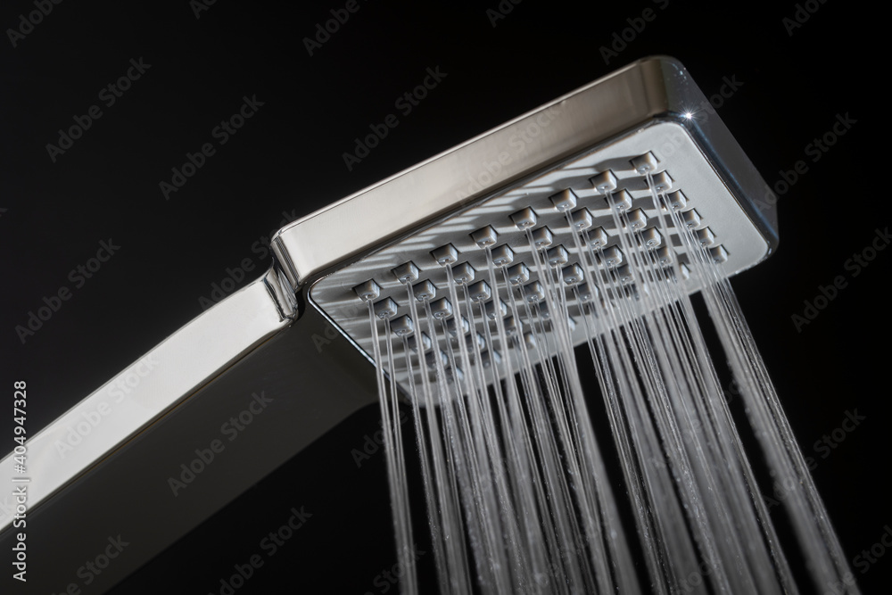 Water running from shower head in bathroom with black background, close up Water running from shower head in bathroom with black background, close up