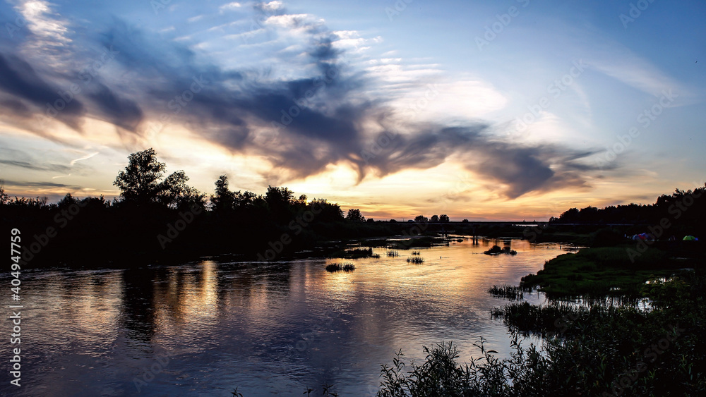 incredible mysterious amazing swirls of clouds at sunset on the river with reflection in the water on a warm summer evening. in the background - a bridge over the river and a tent camp on the river incredible mysterious amazing swirls of clouds at sunset on the river with reflection in the water on a warm summer evening. in the background - a bridge over the river and a tent camp on the river