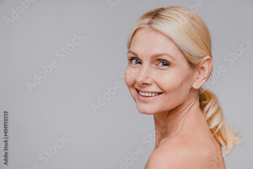 Side view portrait of good-looking mature blonde woman with clean skin smiling isolated over grey background photo