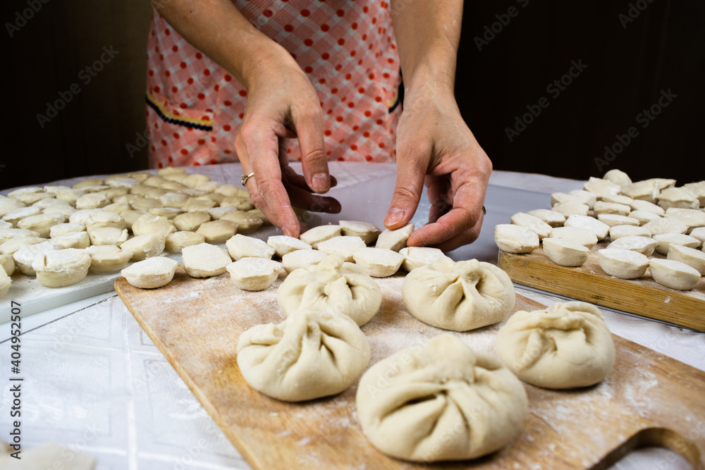 Woman's hands, soiled in flour, neatly lay out handmade, freshly made dumplings, ravioli and khinkali on cutting boards. Woman's hands, soiled in flour, neatly lay out handmade, freshly made dumplings, ravioli and khinkali on cutting boards.