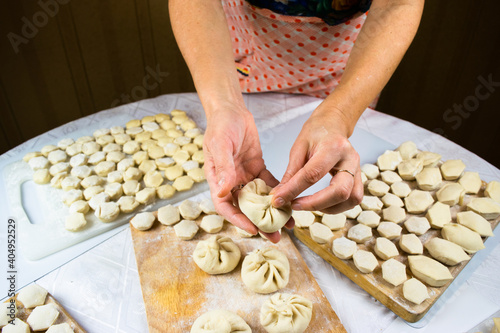 Woman's hands sculpt khinkale dumplings on background of cutting boards with hendmade dumplings, ravioli and khinkali. photo