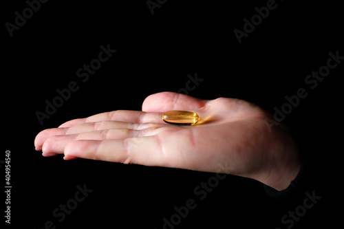 Yellow gel capsule of vitamin D, E, omega-3 in womans hand close-up, black background. Care, health, healthy nutrition