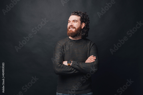 Obraz na plátně Handsome man with beard and long curly hair standing over dark background with crossed arms and looking away