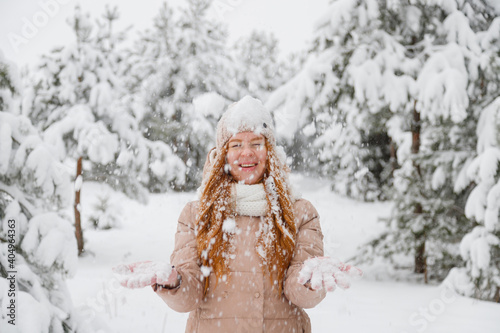 Happy young redhead woman plays with snow in pine tree forest