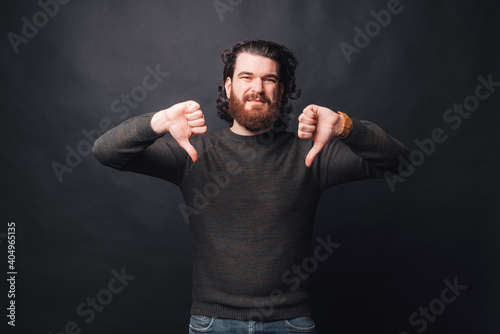 Photo of sad bearded man showing thumbs down over dark background. © Vulp