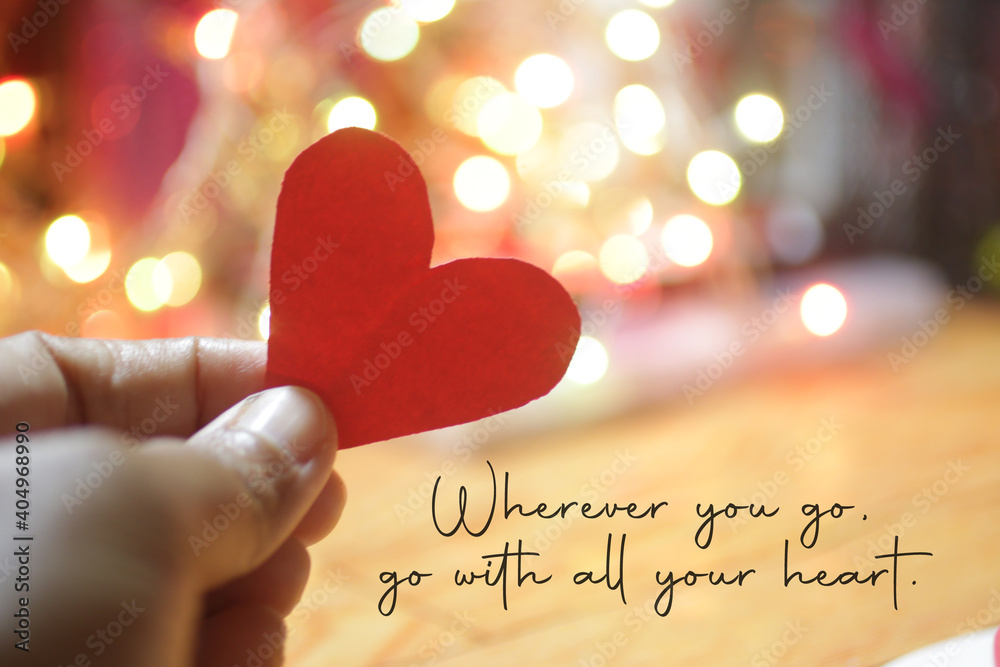 Inspirational quote - Wherever you go, go with all your heart. On pink and white bokeh light background with hand holding red love paper shape. Believe in your heart intuition concept. - obrazy, fototapety, plakaty 