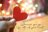Inspirational quote - Wherever you go, go with all your heart. On pink and white bokeh light background with hand holding red love paper shape. Believe in your heart intuition concept.
