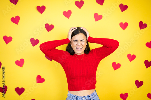 Fotografie Young caucasian woman over yellow background with red hearts suffering from head