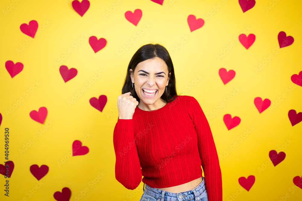 Young caucasian woman over yellow background with red hearts angry and mad raising fist frustrated and furious while shouting with anger. Rage and aggressive concept. Young caucasian woman over yellow background with red hearts angry and mad raising fist frustrated and furious while shouting with anger. Rage and aggressive concept.