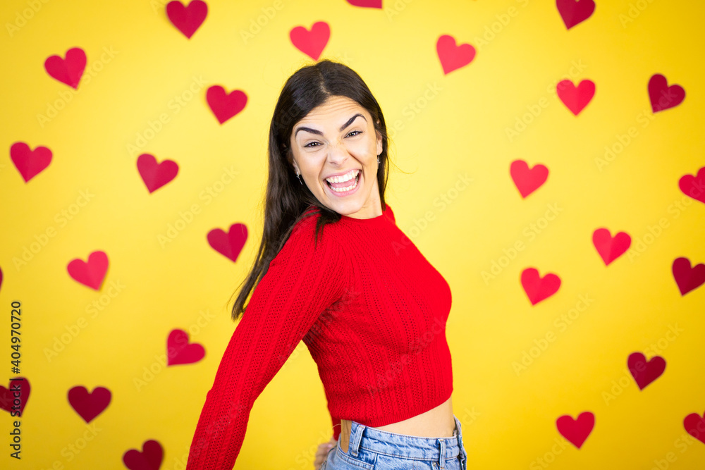 Young caucasian woman over yellow background with red hearts shouting, holidays concept. Young caucasian woman over yellow background with red hearts shouting, holidays concept.