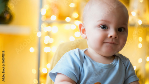 Portrait of 9 month old caucasian baby indoors. Little baby boy smiling, festive bokeh lights on background. Copy space, banner 16x9.
