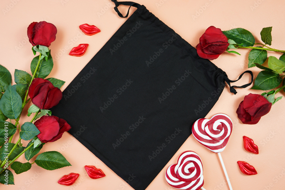 Φωτογραφία Happy Valentine's Day black cotton gift bag, styled with Valentine red roses, heart shape gift and lipstick kissess chocolates on a modern coral background