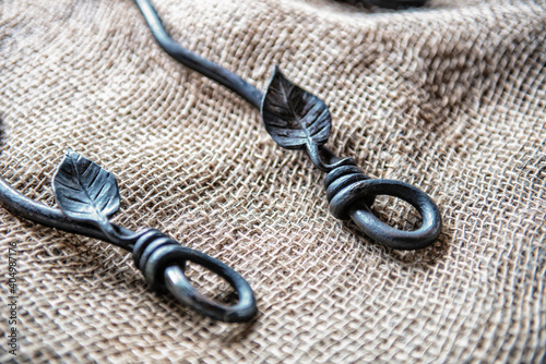 Two decorative wrought iron handles laying on a piece of brown burlap material. The handles have unique leaf patterns with a small curl or loop at the top. The black iron is smooth with a matt finish. photo