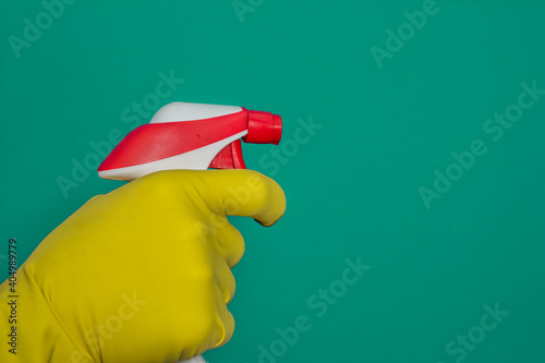 Hand in yellow rubber glove holding plastic spray bottle with cleaning detergent on green background
