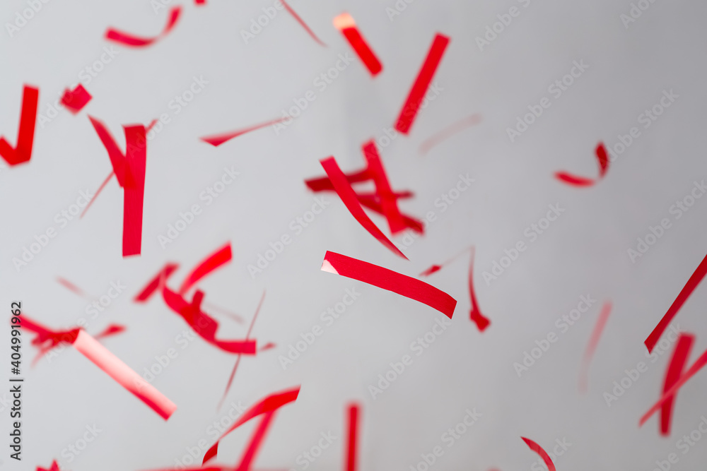Shiny red confetti falling down on light grey background Shiny red confetti falling down on light grey background