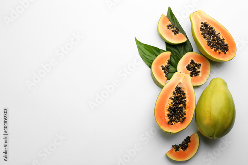 Fototapeta Naklejka Na Ścianę i Meble -  Fresh ripe papaya fruits with green leaves on white background, flat lay. Space for text