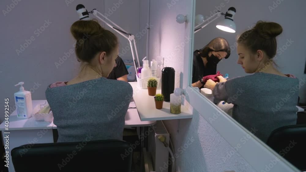 The master of manicure under a table lamp makes a hardware manicure. The client is bored and she turns her head to the side, looking at the details in the cabin. View in the mirror The master of manicure under a table lamp makes a hardware manicure. The client is bored and she turns her head to the side, looking at the details in the cabin. View in the mirror