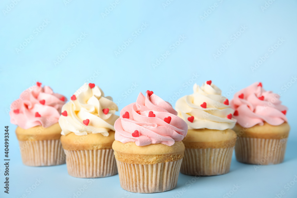 Tasty cupcakes with heart shaped sprinkles on light blue background. Valentine's Day celebration