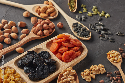 Different kinds of nuts, dried fruits in wooden spoones and dish on black slate background. Top view. Healthy food. Vegetarian nutrition photo