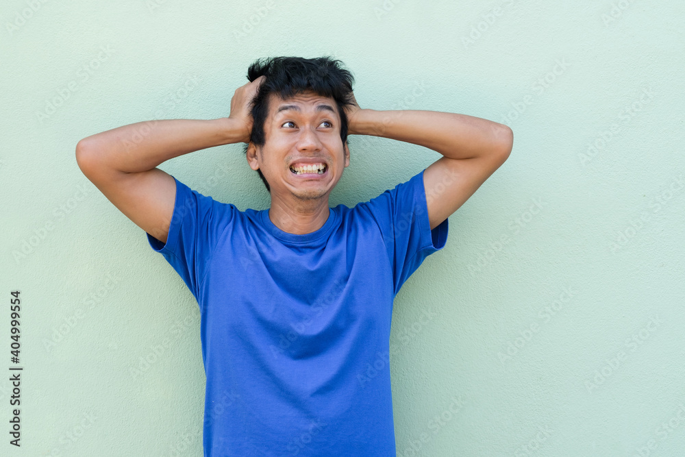 Asian man with worry shock overacting face and raise up hands on head looking top clean background Asian man with worry shock overacting face and raise up hands on head looking top clean background
