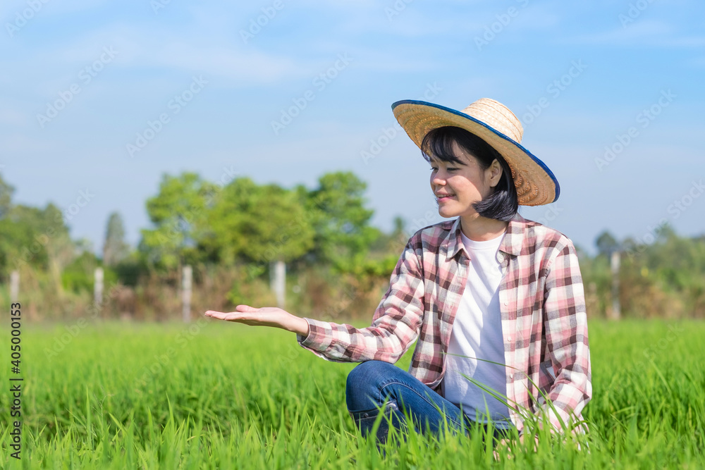 asian farmer woman sitting and raise hand for present products at green rice farm