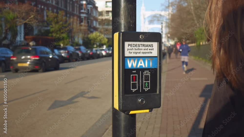 A girl crossing a Pelican crossing - pedestrian light controlled crossing in 4K. Pedestrian presses the button and crosses a street. Push button and wait for signal opposite, wait signal.
