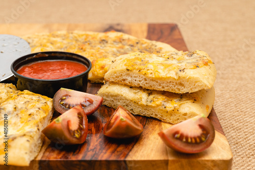 Classic cheesy bread topped with herb garlic spread, and cheese blend served with marinara sauce and fresh sliced tomatoes close up on rustic background
