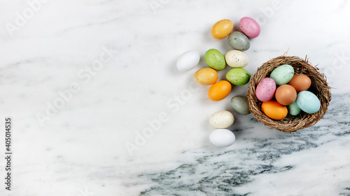 Happy Easter concept with basket of colorful eggs and nest on stone background in flat lay format