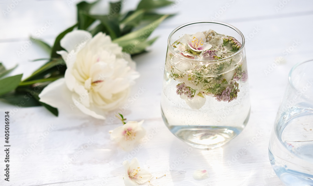 glass with floral infused drink. non alcohol mocktail for summer refresh. outdoors summer party. flower ice cubes in a glass. summer herbal drink concept. glass with floral infused drink. non alcohol mocktail for summer refresh. outdoors summer party. flower ice cubes in a glass. summer herbal drink concept.