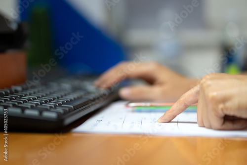 Close-up action of at person's finger in pointing to correct the data on paper with blurred background of the another hand typing on keyword to input data in computer. Business working photo. photo
