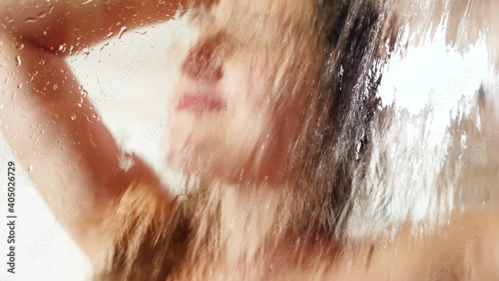 Portrait through wet shower glass on smiling happy woman washing hair and relaxing in shower. Concept of female beauty, body care and healthcare during pregnancy. Portrait through wet shower glass on smiling happy woman washing hair and relaxing in shower. Concept of female beauty, body care and healthcare during pregnancy.