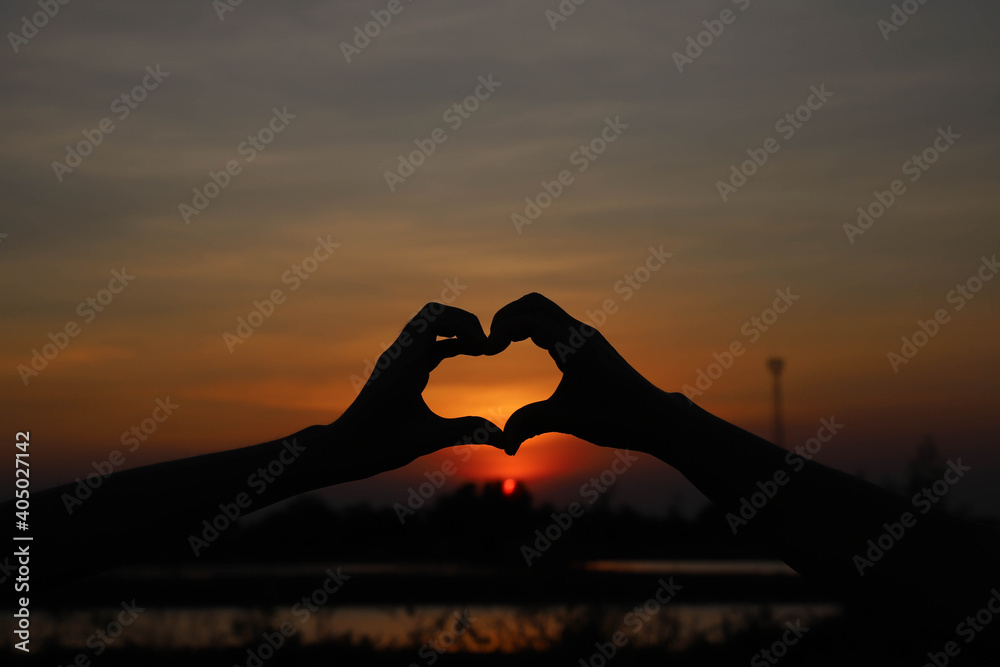 Young men and women Make a heart shaped hand to show love in the silhouette.