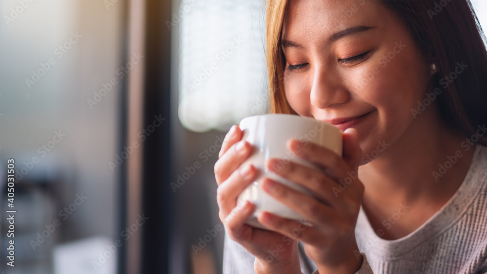 Closeup image of a beautiful young asian woman holding and drinking hot coffee in cafe Closeup image of a beautiful young asian woman holding and drinking hot coffee in cafe