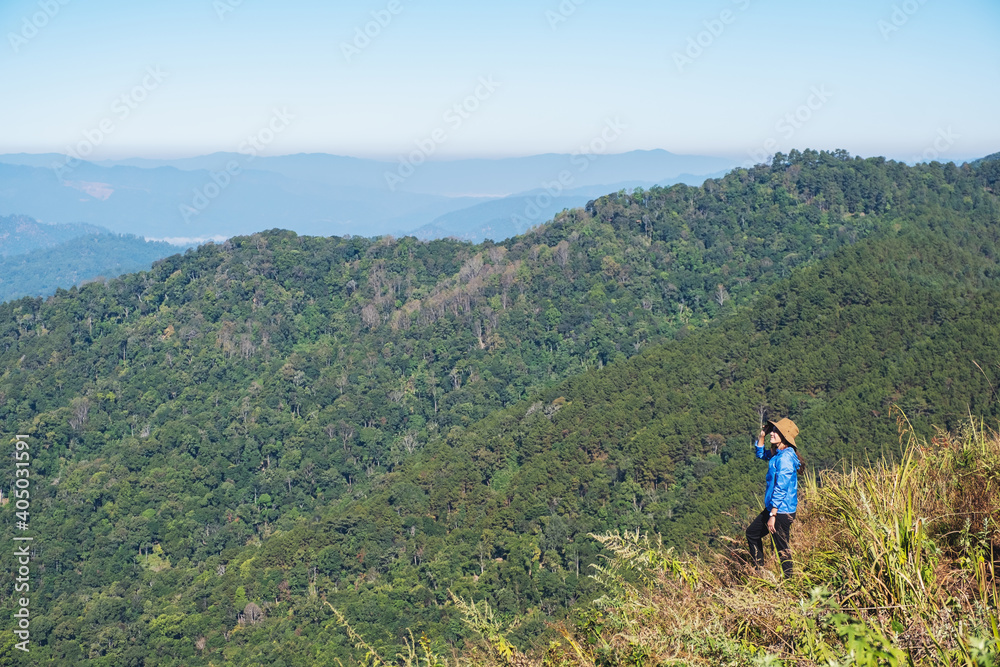 A female traveler hiking and sitting on mountain peak, looking at a beautiful view