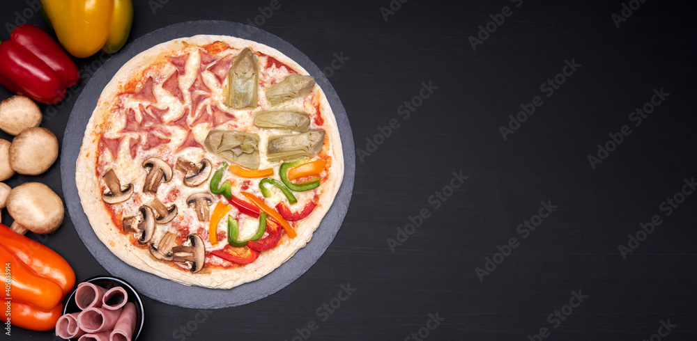 four seasons pizza (quattro stagioni) made with tomato sauce, mozzarella cheese, ham, artichokes, peppers and mushrooms on a stone plate with a black background with copy space for advertising. 