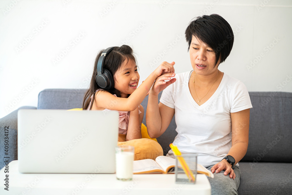 Asian girl homeschooling with her mother using laptop computer and online learning at home wile coronavirus or covid-19 outbreak situation. Homeschooling, home study or online learning concept Asian girl homeschooling with her mother using laptop computer and online learning at home wile coronavirus or covid-19 outbreak situation. Homeschooling, home study or online learning concept