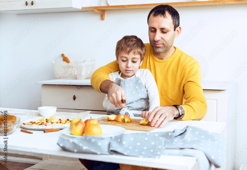 Small adorable kid boy preparing apple pie with caring father on domestic kitchen.