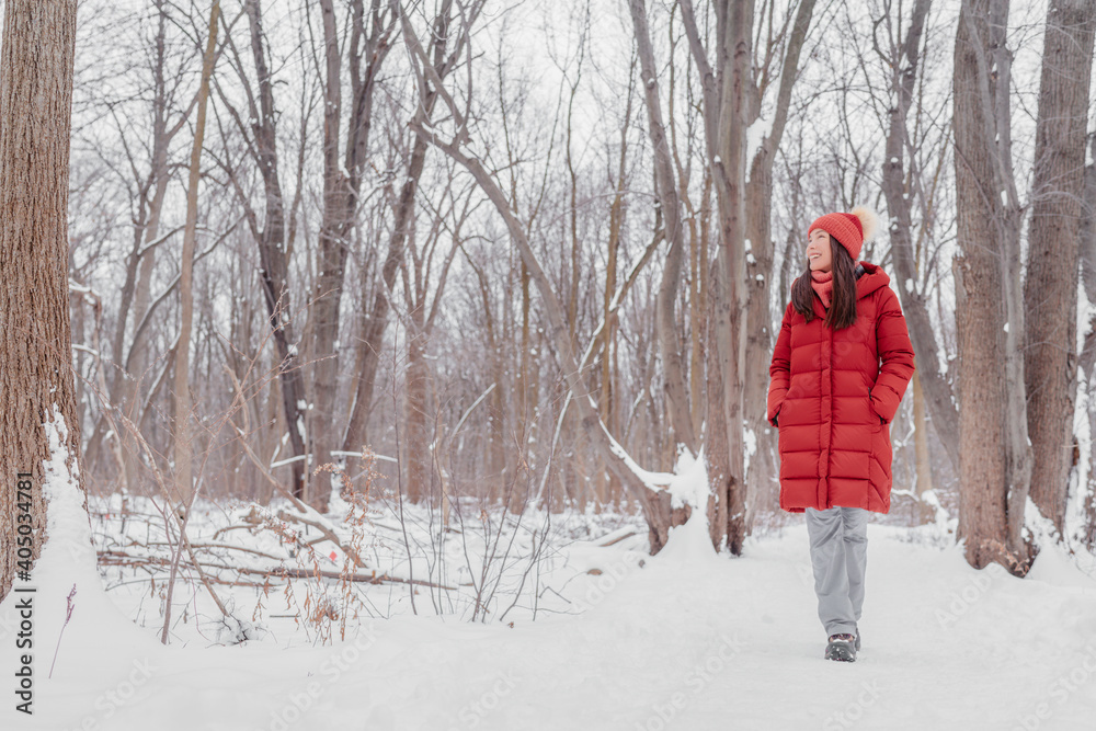 Happy Asian girl walking in snow path. Woman in red coat doing outdoor winter activity enjoying cold season.