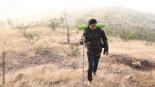 Wide angle full shot of Hiker with stick climbing the mountain hill top during foggy cold morning - concept of solo hiking or trekking.concept of solo trravel and trekking. photo