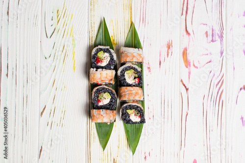 Top view of Japanese black rice sushi roll with shrimp on top served on bamboo leaves on colorful light wooden background. Avocado wrapped in black rice 