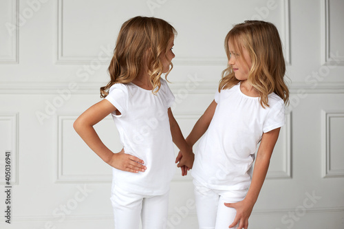 Two little kids girls in white clothes, over white background children studio portrait. Twin girls look each other.