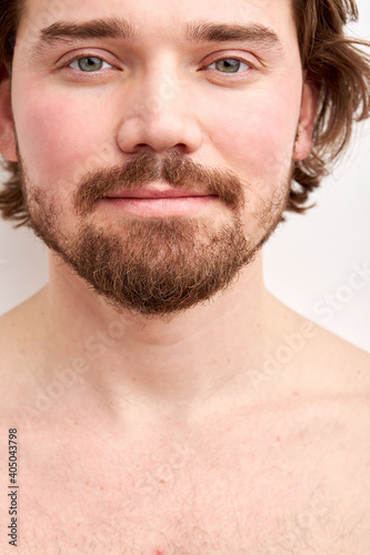 shirtless man model with stylish haircut posing at camera isolated on white background, bearded male has natural expression, calm and confident look