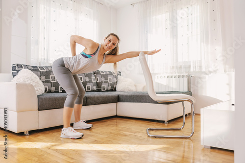 Muscular sportswoman in shape doing fitness exercises for her backs while leaning on chair. If you can't go to the gym, you can make your own at home.