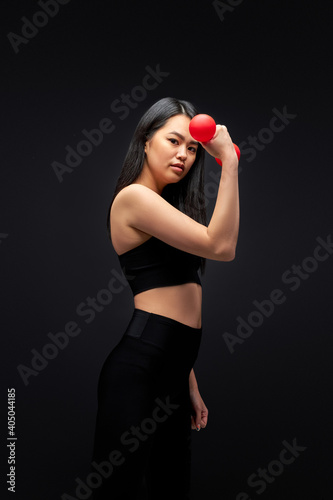 asian woman in black sportive wear with dumbbells, pumping arm muscles, isolated on black studio background. sport and healthy lifestyle concept