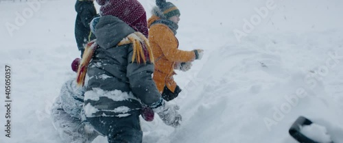 HANDHELD Group of kids having snowball fight brawl, hiding behind the snow fort wall. Fun winter games outside. 120 FPS slow motion shot photo