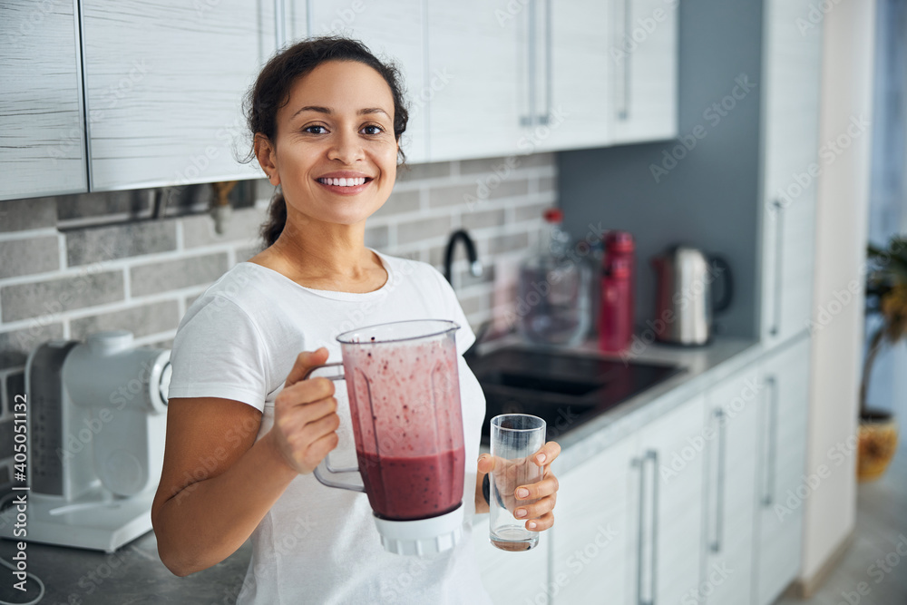 Joyous housewife with a fruit smoothie smiling at the camera Joyous housewife with a fruit smoothie smiling at the camera